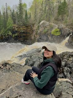 a woman sitting on top of a large rock next to a river filled with water