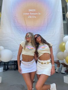 two women standing next to each other in front of a sign