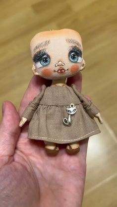 a hand holding a doll with blue eyes and brown dress on it's fingers