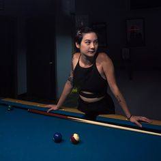 a woman standing next to a pool table in a dark room with balls on it