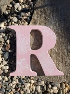 a pink wooden letter sitting on top of a pile of rocks next to a rock