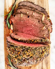 sliced roast beef on a cutting board with rosemary sprigs and seasoning next to it