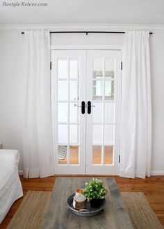 a living room with white curtains and a coffee table in front of the glass doors