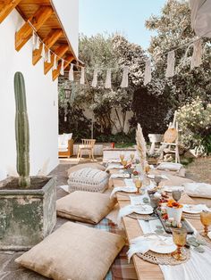 an outdoor table set up with place settings and cactus in the backgrouf