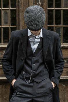 a man in a suit and tie with a hat on his head standing next to a door