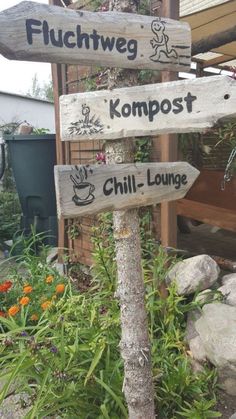 several wooden signs pointing in different directions on a pole next to some rocks and flowers