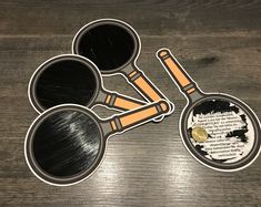 three metal pans with black and orange handles on top of a wooden table next to each other