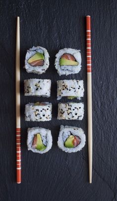 sushi rolls with avocado and sesame seeds on a black surface next to chopsticks