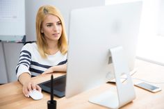 a woman sitting at a desk with a computer monitor and mouse in front of her