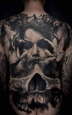 a man's back with tattoos on his body and skull in the middle of it