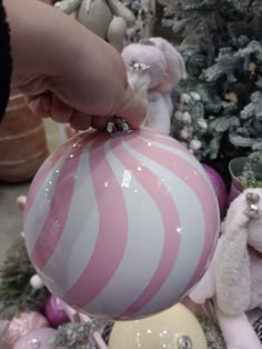 a person holding a pink and white striped ball ornament in front of christmas trees