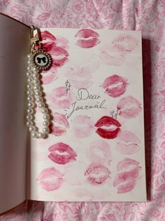 an open book with pink lipstick on it and a pearl charm hanging from the cover