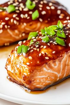 two pieces of salmon on a plate with sesame seeds and green garnishes