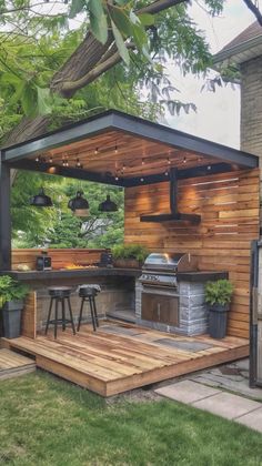 an outdoor kitchen is built into the side of a house with wooden decking and bar stools