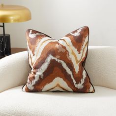 a brown and white pillow sitting on top of a white couch next to a lamp