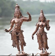 two bronze statues are standing next to each other on a dock near the water and trees