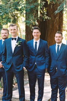 a group of men in suits standing next to each other on a wooden walkway surrounded by trees