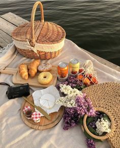 a picnic table with bread, jams and donuts on it next to the water