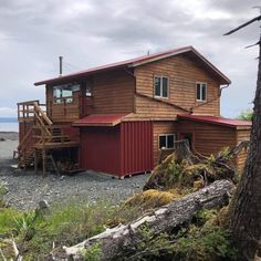 a red and brown house sitting on top of a lush green hillside next to the ocean