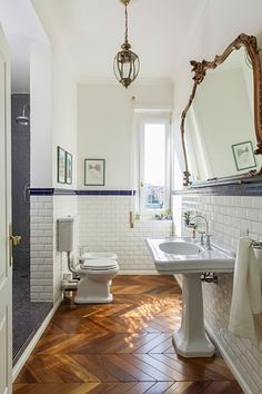 a bathroom with white walls and wood flooring next to a sink, toilet and mirror