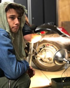 a young man sitting next to a motorcycle