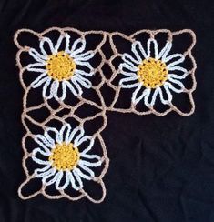 three crocheted flowers sitting on top of a black cloth covered in white and yellow yarn