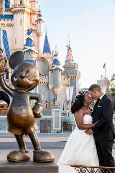 a bride and groom kissing in front of mickey mouse statue at disney's castle