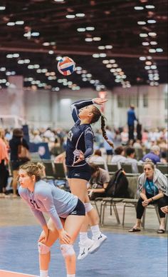 two girls are playing volleyball in an indoor court while people watch from the sidelines