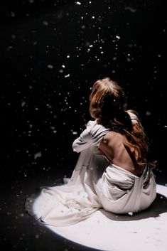 a woman sitting on top of a white floor covered in snow next to a black background