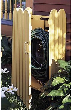 a yellow fence with a hose hooked up to it in front of some flowers and bushes