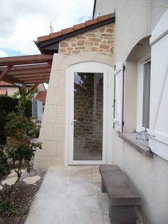 an outside view of a house with a stone wall and white door, bench in the foreground