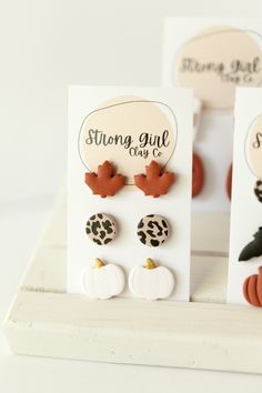 three pairs of earrings on display in front of white cards with black and orange designs