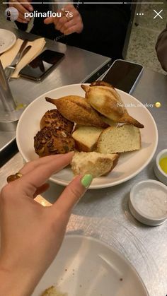 a person is pointing at some food on a plate with bread and other foods in the background