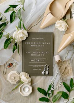 the wedding stationery is laid out with shoes, jewelry and flowers on top of it