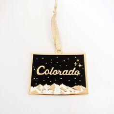 a black and gold colorado ornament hanging on a white wall with stars in the sky