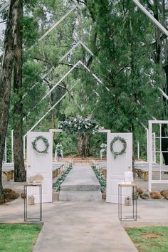 an outdoor ceremony setup with white chairs and wreaths on the doors, surrounded by trees