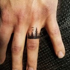 a person's hand with a small tattoo on it and trees in the background