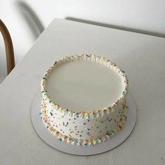 a white cake with sprinkles on it sitting on top of a table