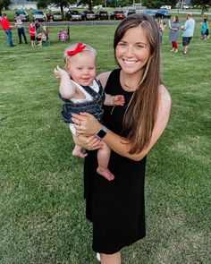 a woman holding a baby in her arms while standing on top of a grass covered field