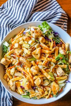 a white bowl filled with pasta salad on top of a wooden table next to a blue and white towel