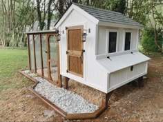 a chicken coop in the middle of a field with gravel around it and a wooden door