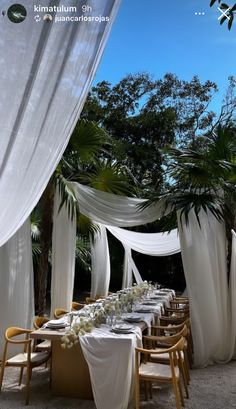 an outdoor dining area with white draping and wooden chairs