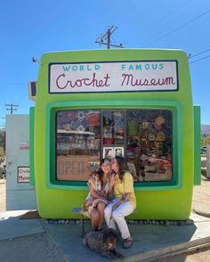 two women sitting on a bench in front of a museum booth with a dog and cat