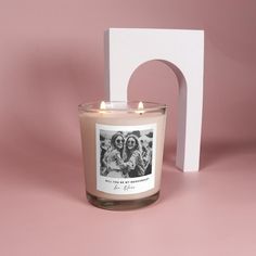 a candle sitting next to a photo frame on a pink surface with a white block in the background