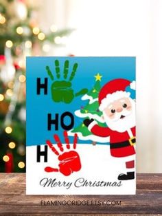 a christmas card with santa clause and handprints on it, next to a christmas tree