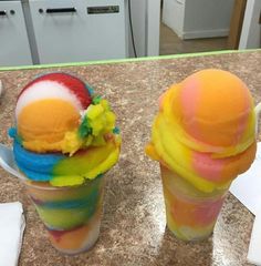 two ice cream cones with different colored toppings sitting on top of a kitchen counter