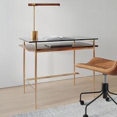 a desk with a chair and lamp on it in front of a white wall next to a rug