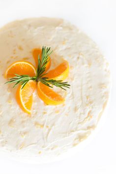 oranges and rosemary sprigs are on top of a white frosted cake