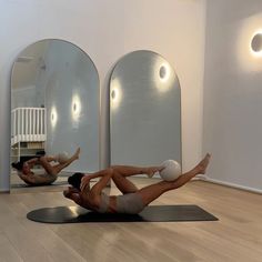 two women doing exercises on yoga mats in front of three mirrors, one with her legs up and the other upside down