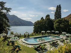 an outdoor swimming pool surrounded by lawn chairs and umbrellas with mountains in the background